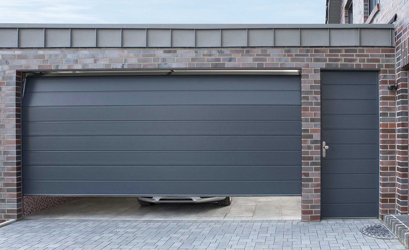 A garage door with a parked car, next to an entrance door, highlighting the craftsmanship of Britannia Garage Doors company.