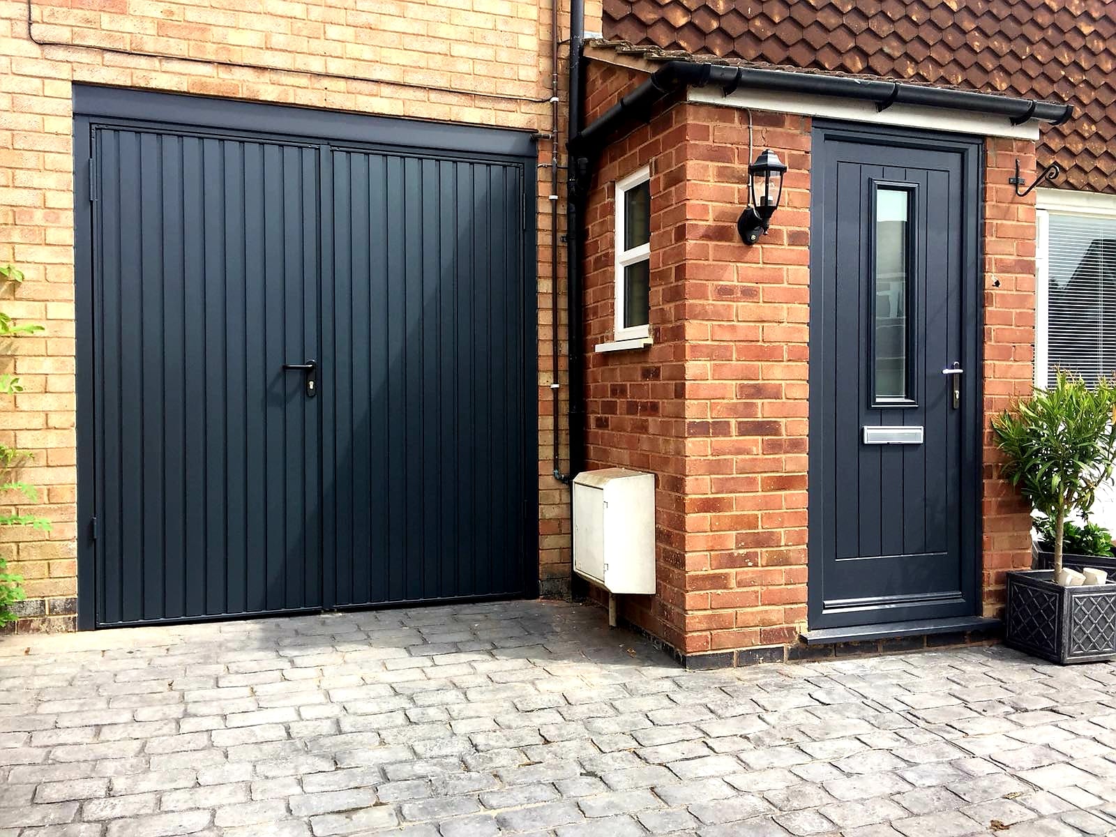 A Britannia garage door and front door, framed by a brick driveway and patio.