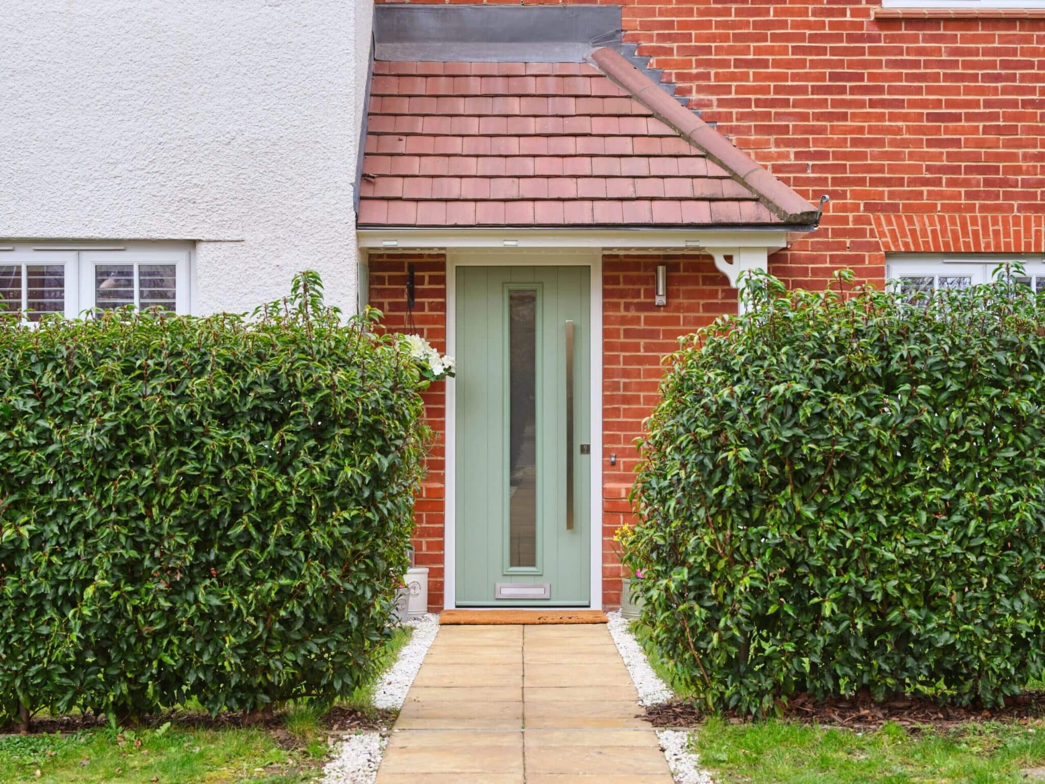A mint green composite front door surrounded by lush green hedges.