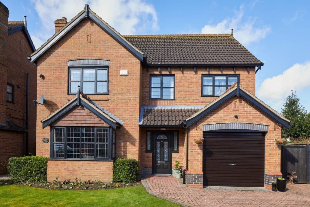 A large brick house with a black garage door, black front door, and a driveway leading up to it.
