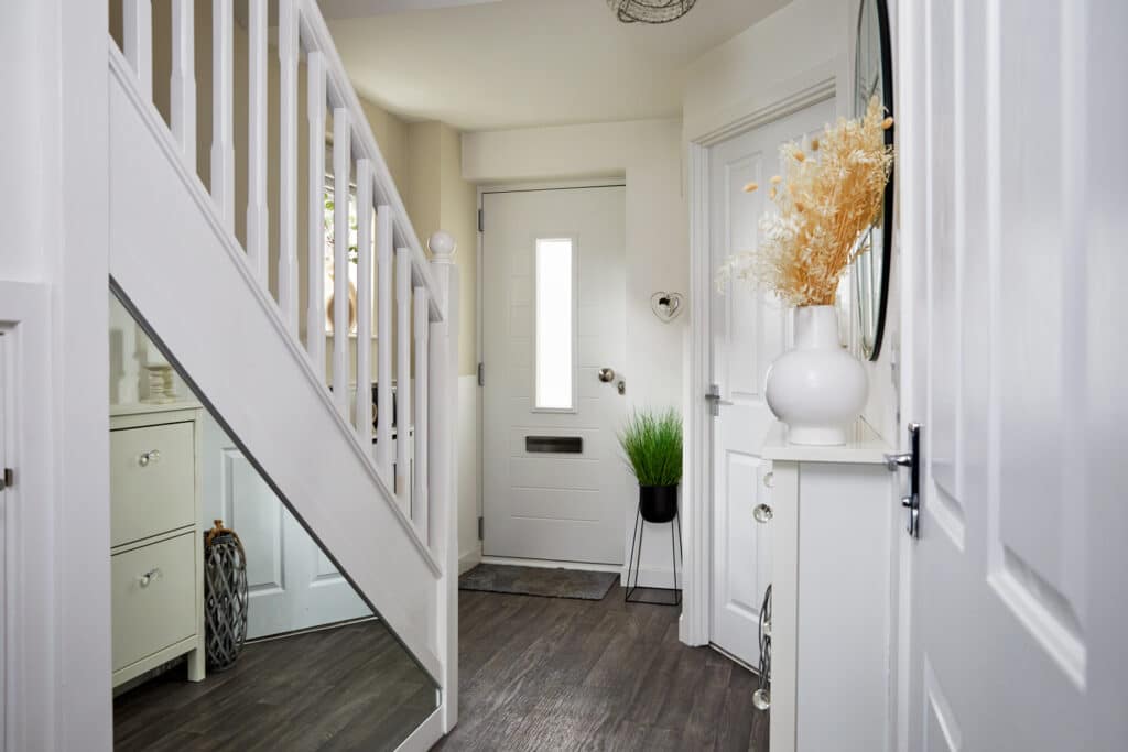 A hallway featuring a mirror, a vase on the floor, and a view of a composite front door.