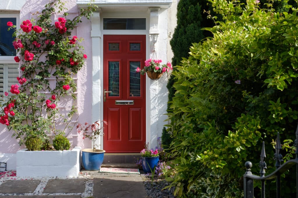 A bright red door on a pink house, adorned with blooming flowers in the garden.