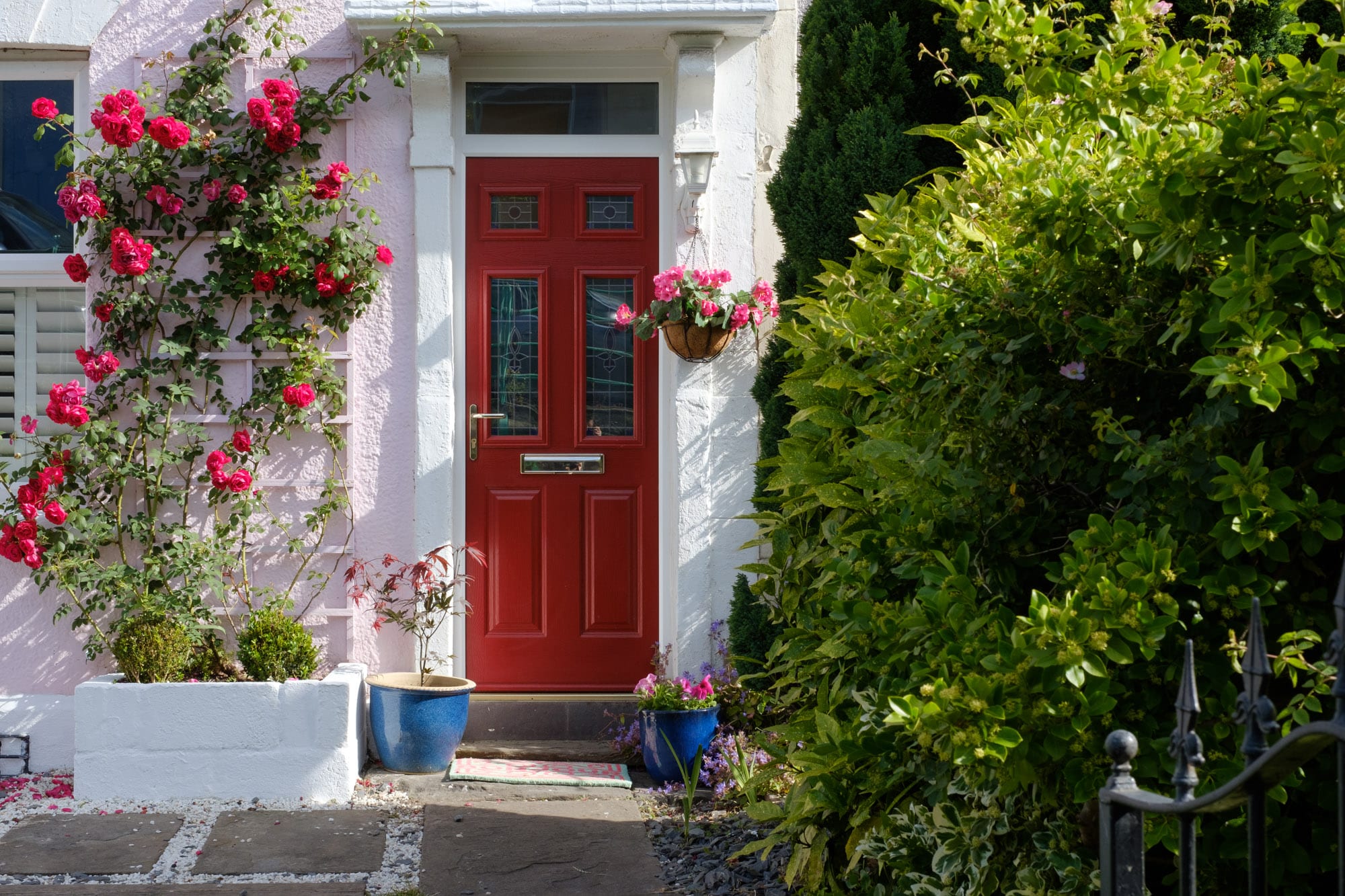 A bright red door on a pink house, adorned with blooming flowers in the garden.